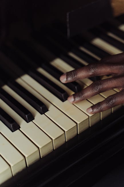 A close-up black-and-white photograph of a piano during a house relocation process, showing its open sheet music stand positioned behind the keyboard. The music stand holds a piece of sheet music with